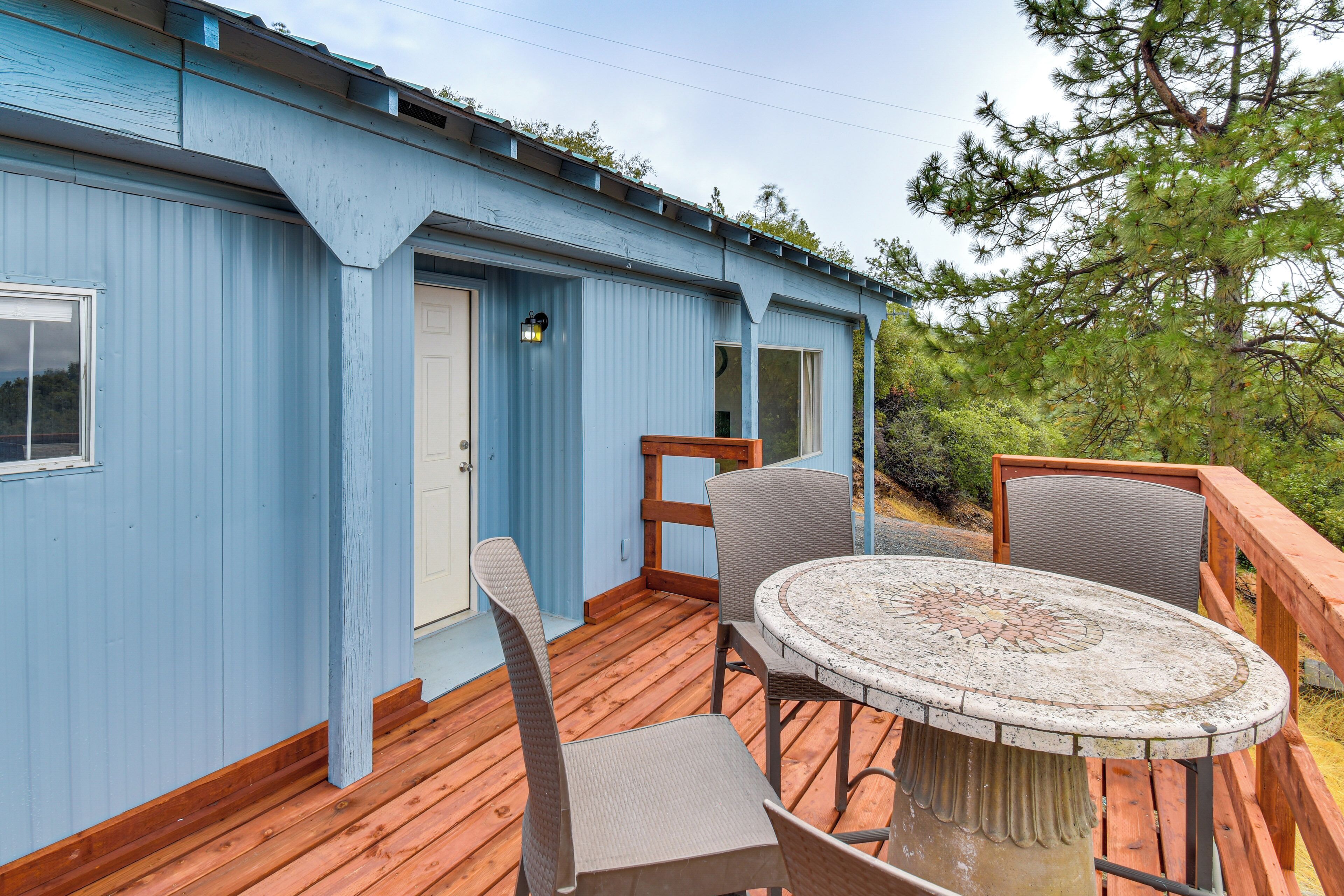 A blue building with a wooden deck, a round table with chairs, and a door.