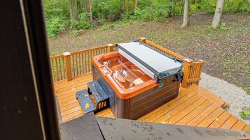 Een hottub op een houten terras met uitzicht op een bos.