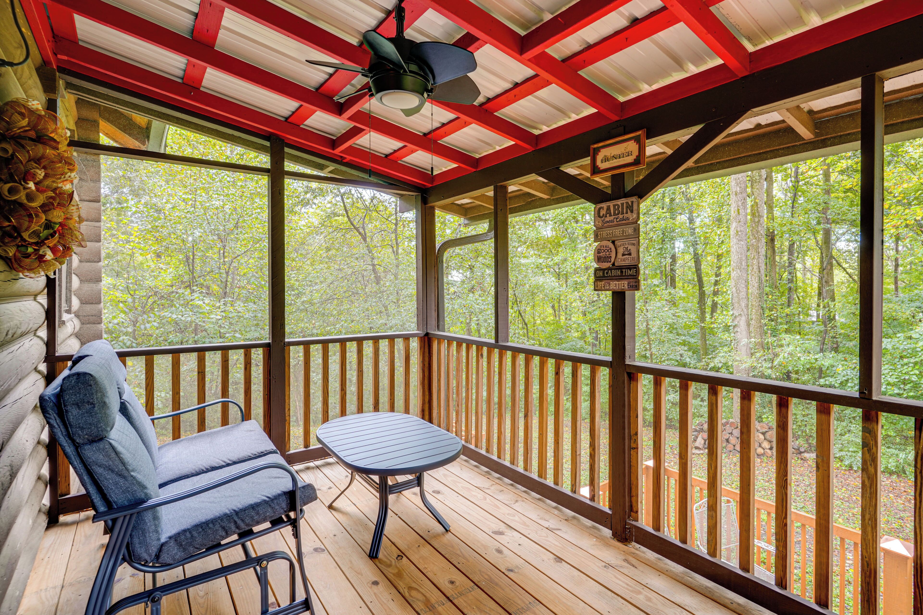 A wooden deck with a table and chair, surrounded by a wooden railing, overlooking a forested area.
