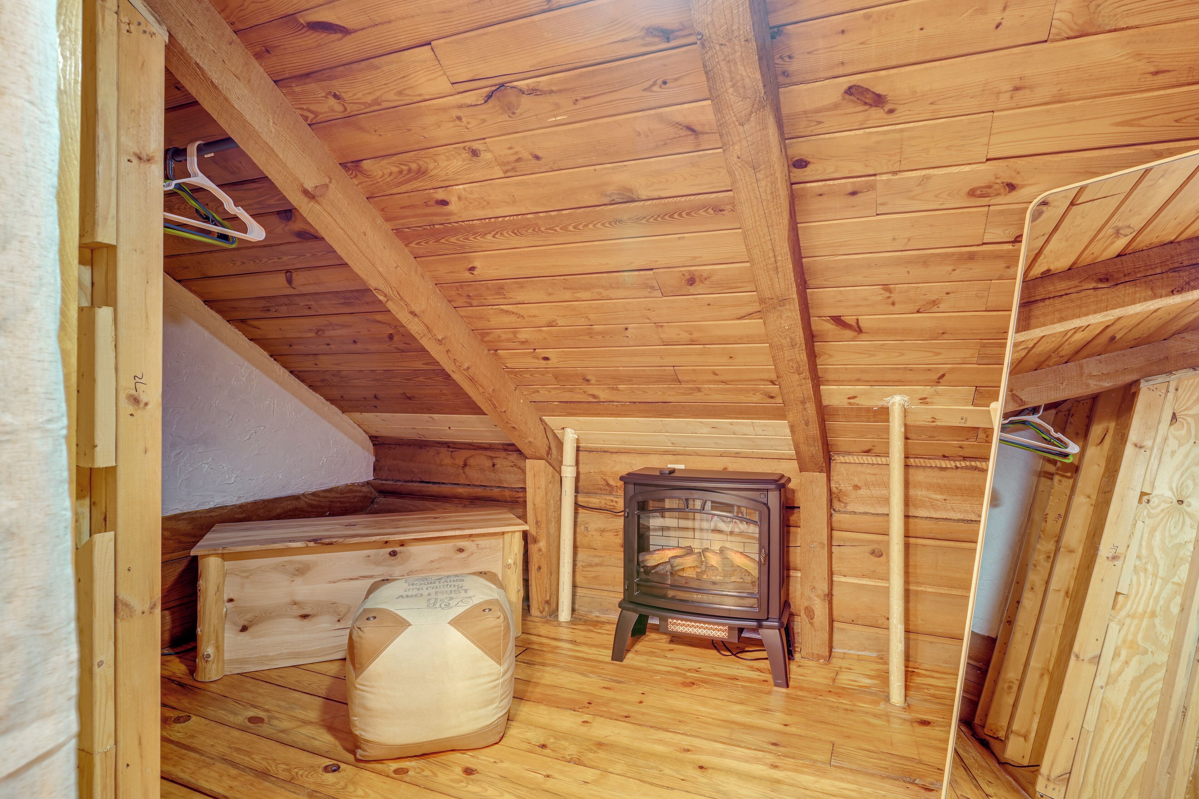 A wooden cabin with a loft bed, a small wooden heater, and a ladder.