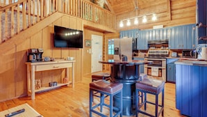 Interior de una cabaña de madera con cocina, comedor y escalera.