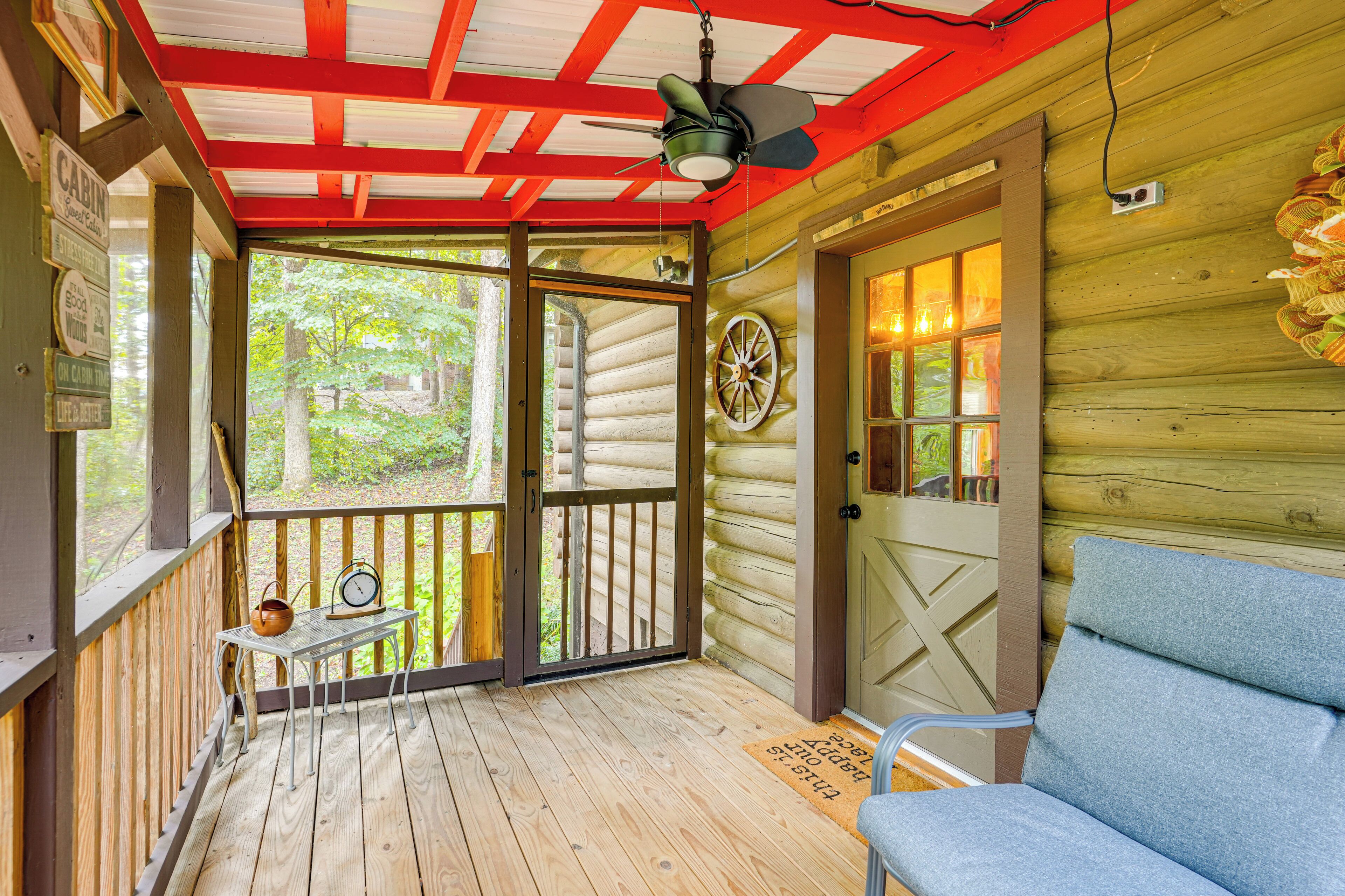 A cabin with a wooden exterior, a porch with a bench, a door with a wheel, and a window with a view of greenery.