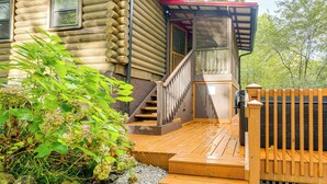 Una cabaña de troncos con terraza de madera, escaleras y un porche cubierto.