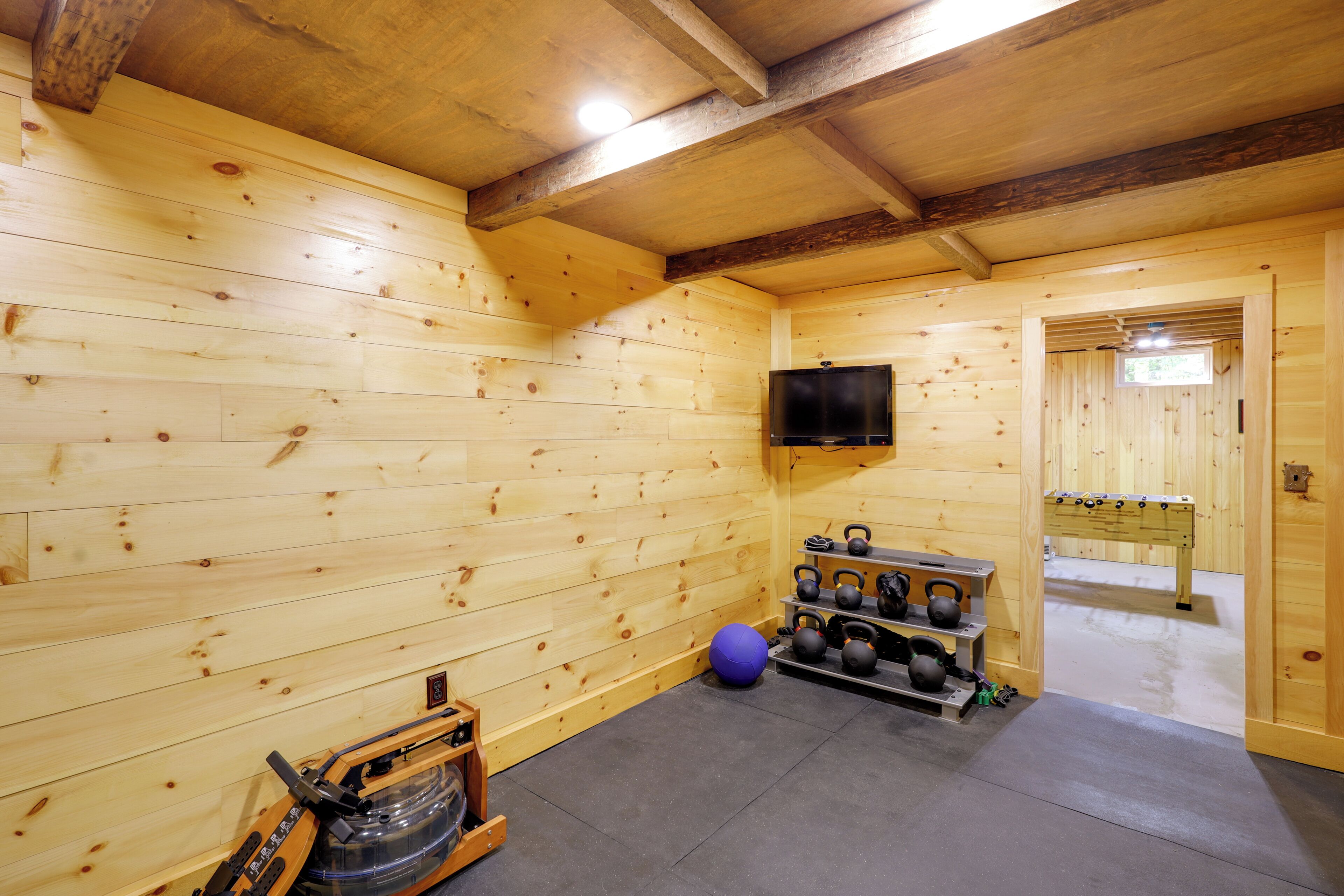 A wooden room with a ceiling fan, a television mounted on the wall, and a rack holding kettlebells and dumbbells.