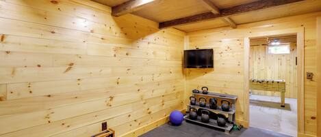 A wooden room with a ceiling fan, a television mounted on the wall, and a rack holding kettlebells and dumbbells.