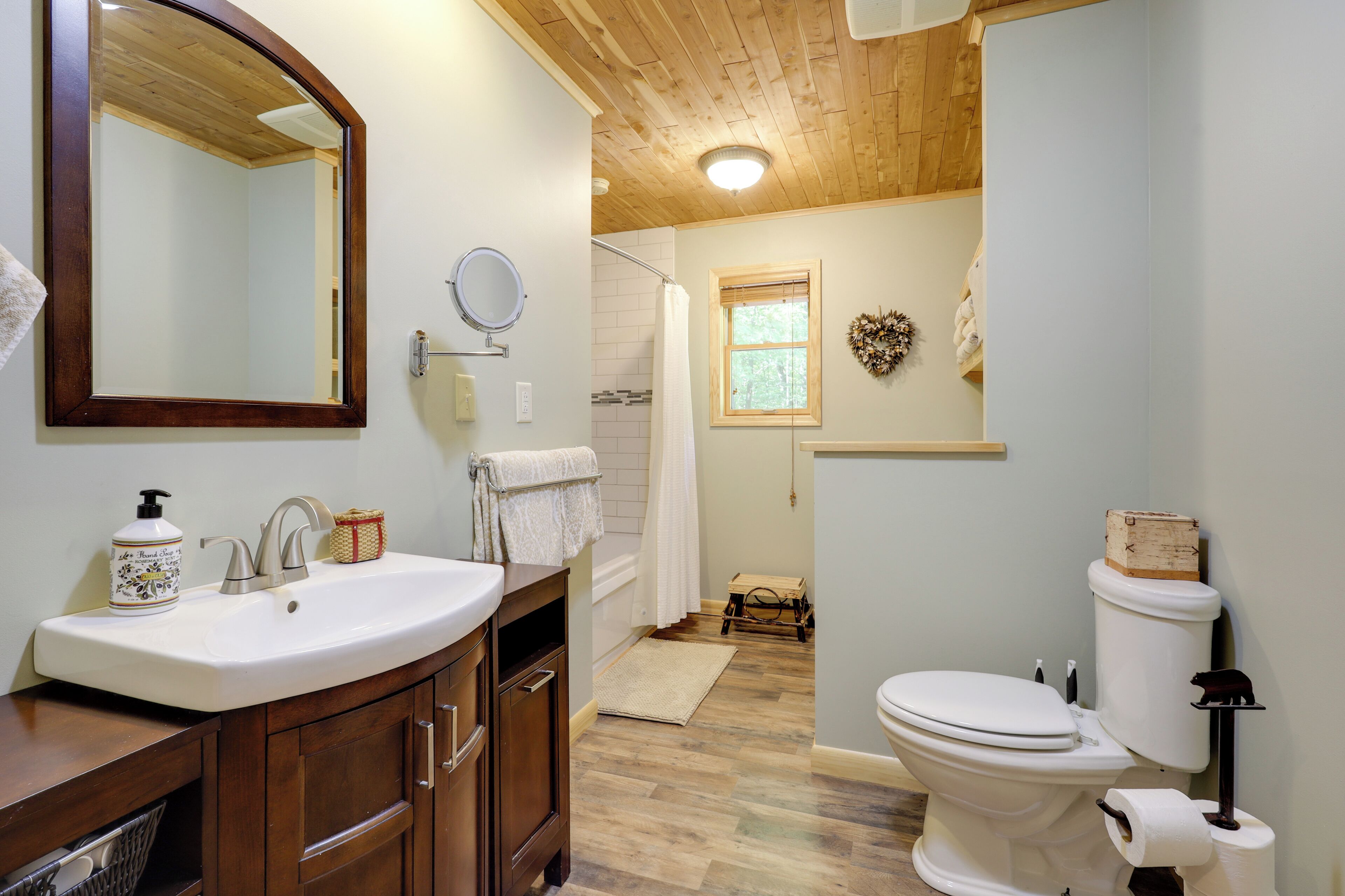 A bathroom with a wooden vanity, a large mirror, a toilet, and a shower area.