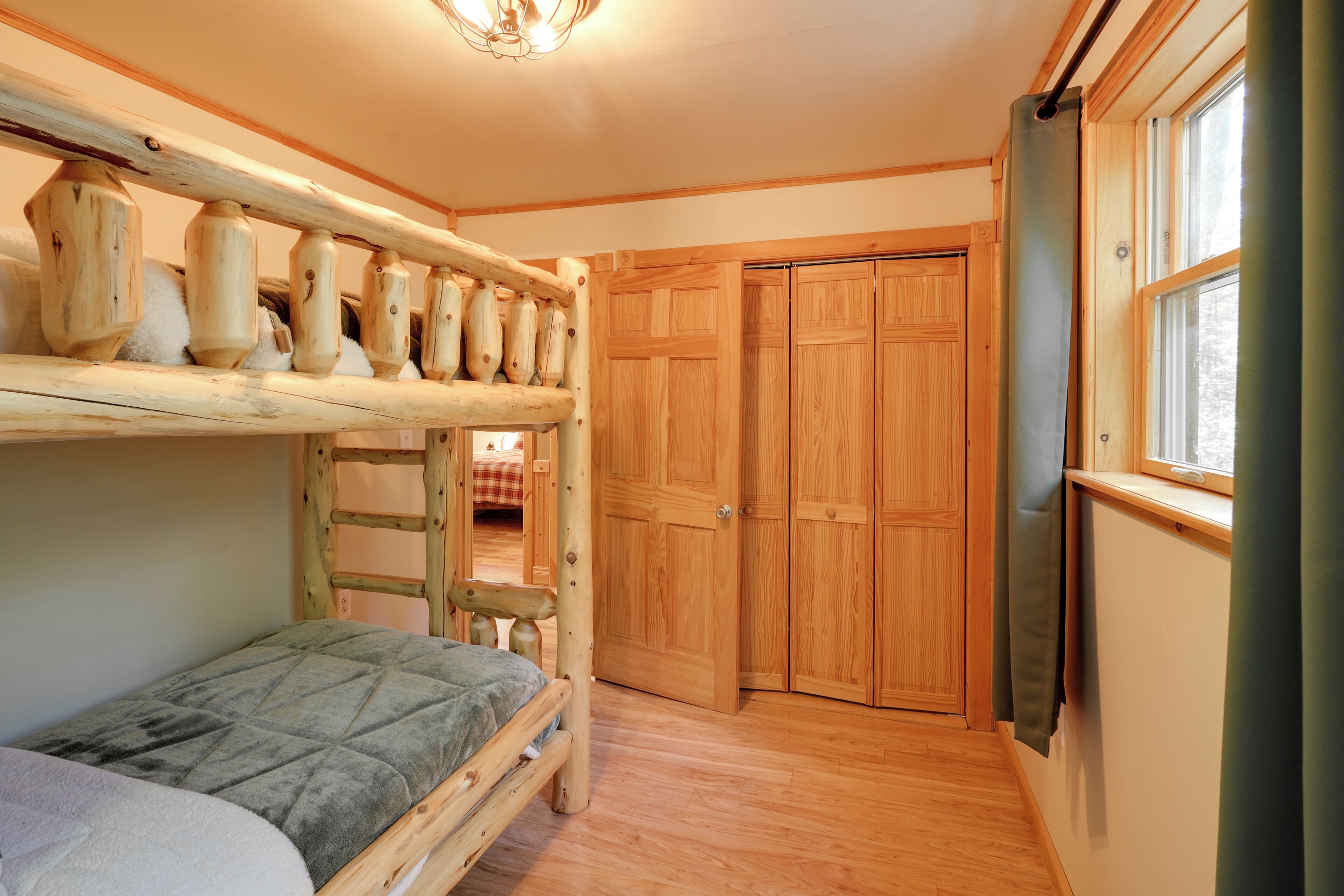 Ein kleines Schlafzimmer mit Etagenbett, Holzschrank und Fenster.