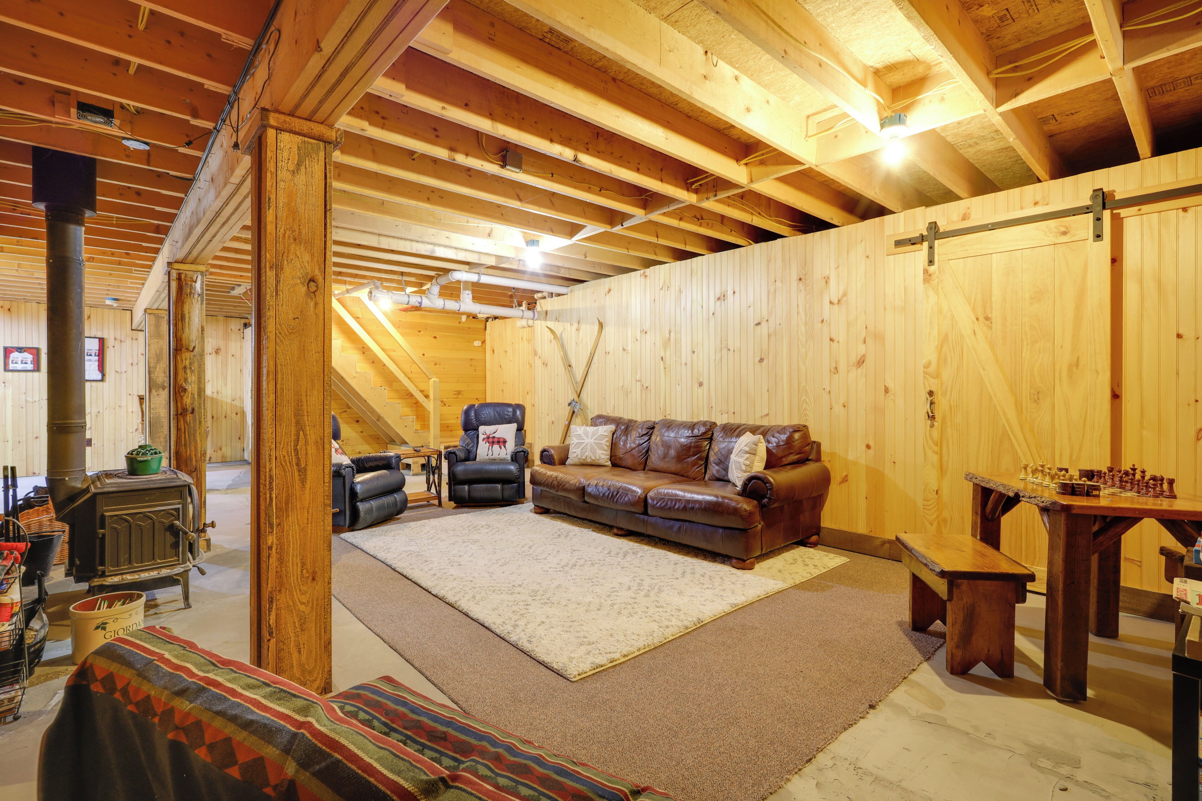 A cozy attic room with a wooden ceiling, a fireplace, a sofa, a table, and a chessboard.