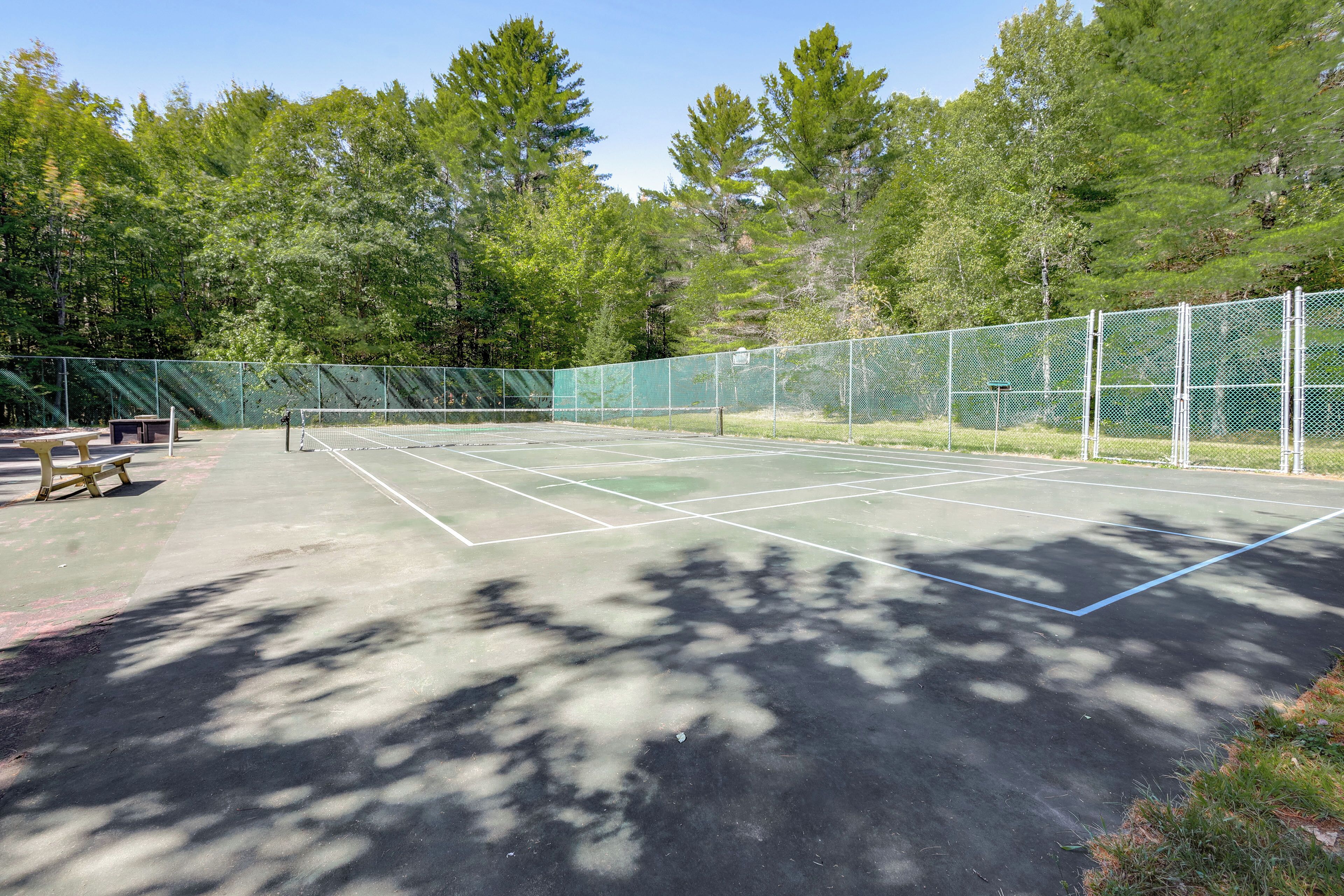 Ein Tennisplatz im Freien mit einem grünen Zaun, Bänken und Bäumen im Hintergrund.