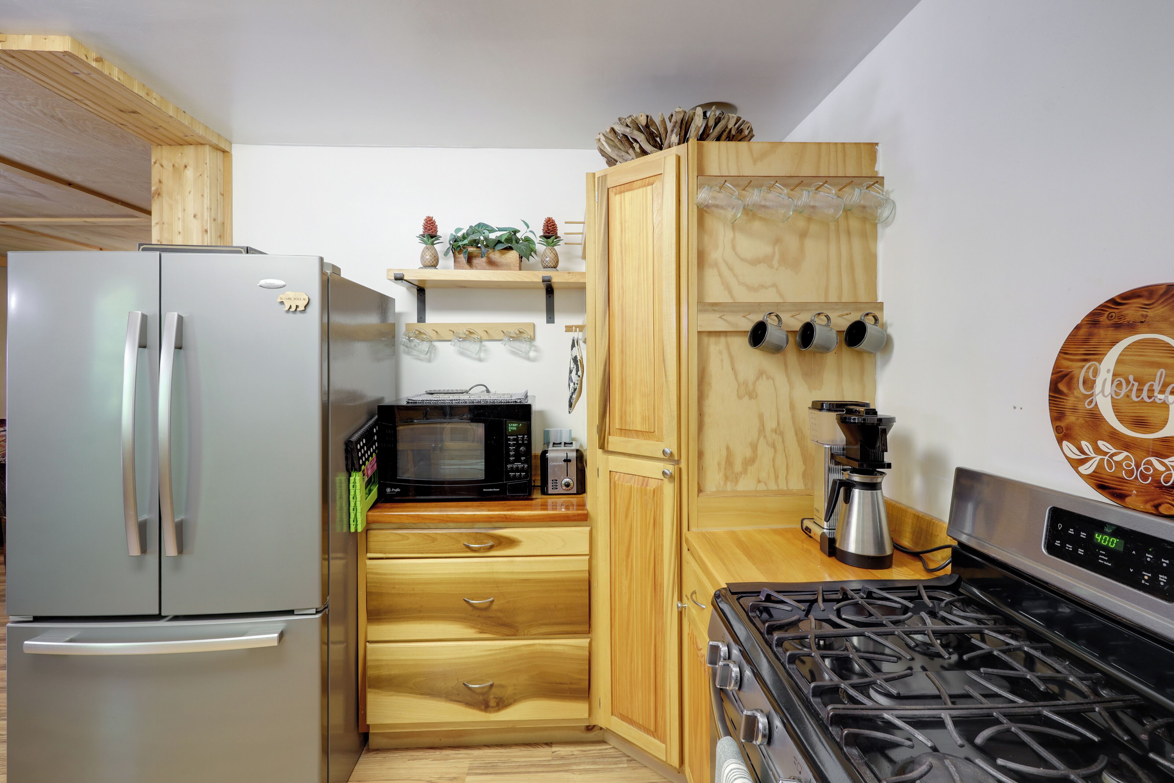 A compact kitchen with a stainless steel refrigerator, a microwave, a stove, wooden cabinets, and a coffee maker.