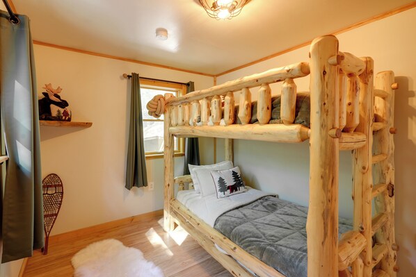 Un lit superposé en bois avec une échelle, une petite étagère décorée d’une image d’un élan, une fenêtre avec des rideaux et un plancher en bois.