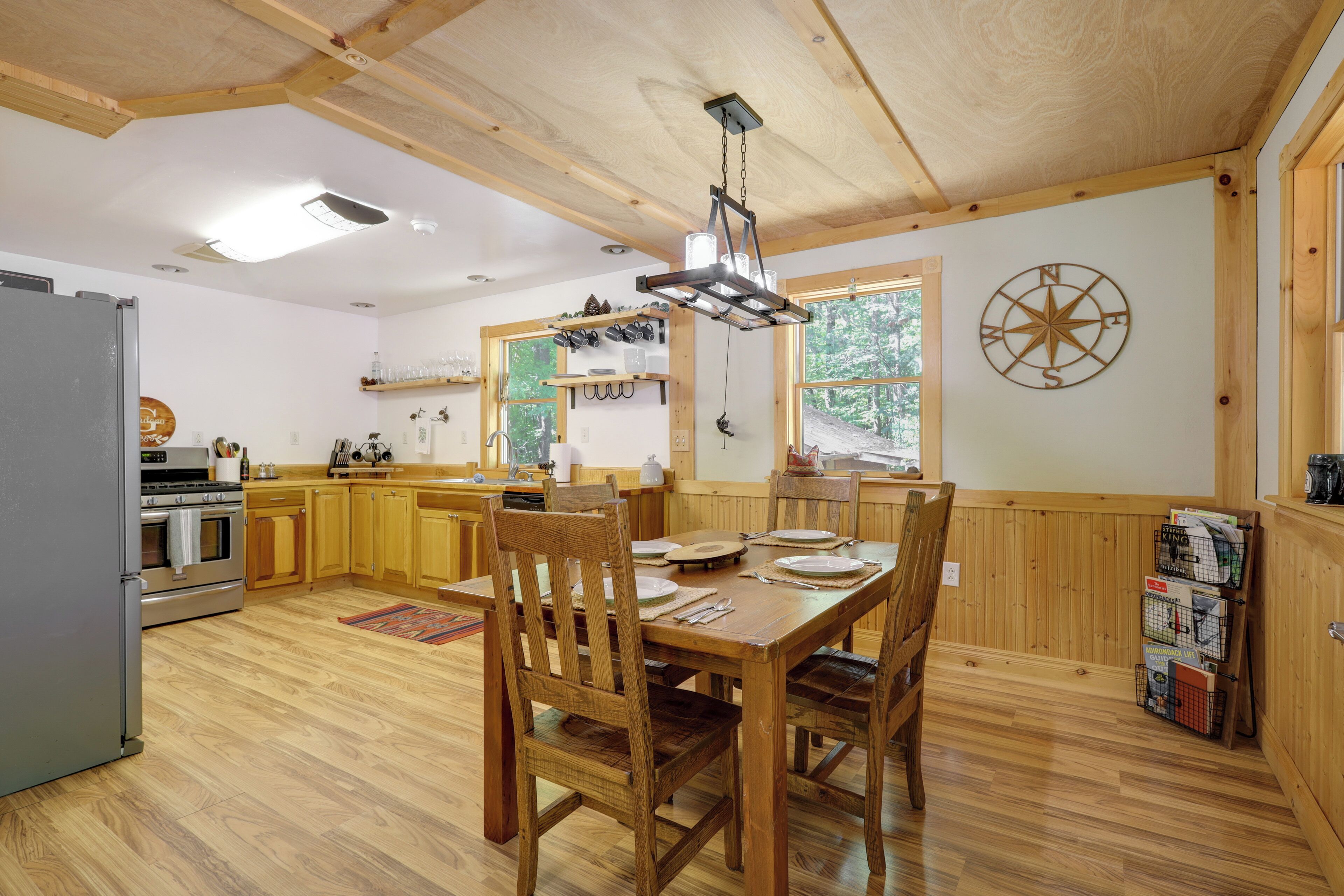 A wooden interior with a dining table, chairs, a kitchen area, and a compass wall decoration.