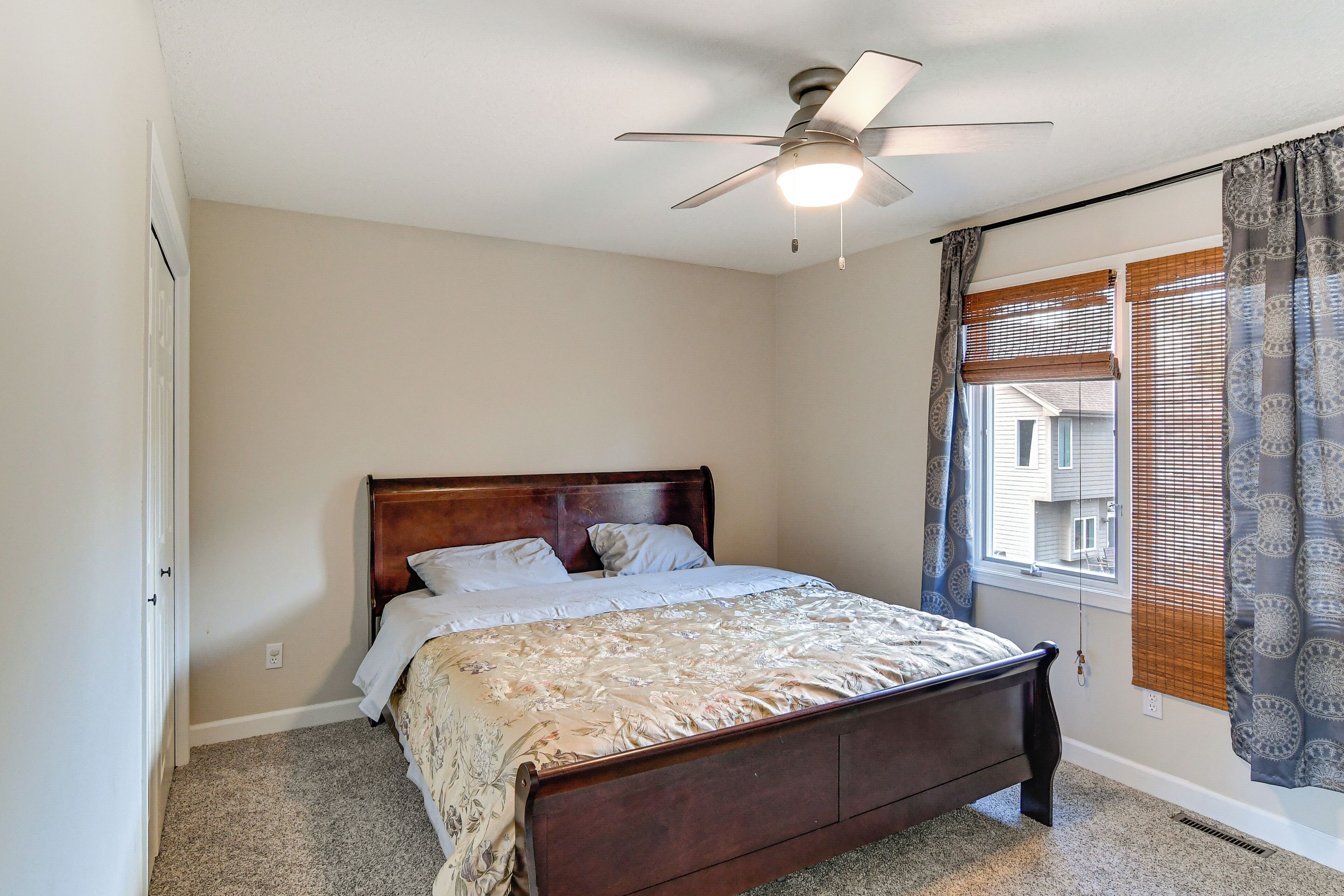 A bedroom with a wooden bed, a ceiling fan, and a window with blinds.