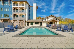 Une piscine entourée de bâtiments dotés de balcons, avec des chaises longues et des tables à proximité, le tout sous un ciel dégagé.
