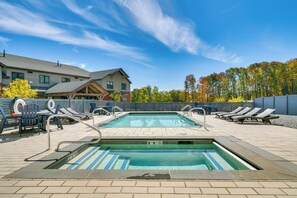 Une piscine dotée de chaises longues et d’une terrasse, entourée d’arbres et avec un bâtiment en arrière-plan.