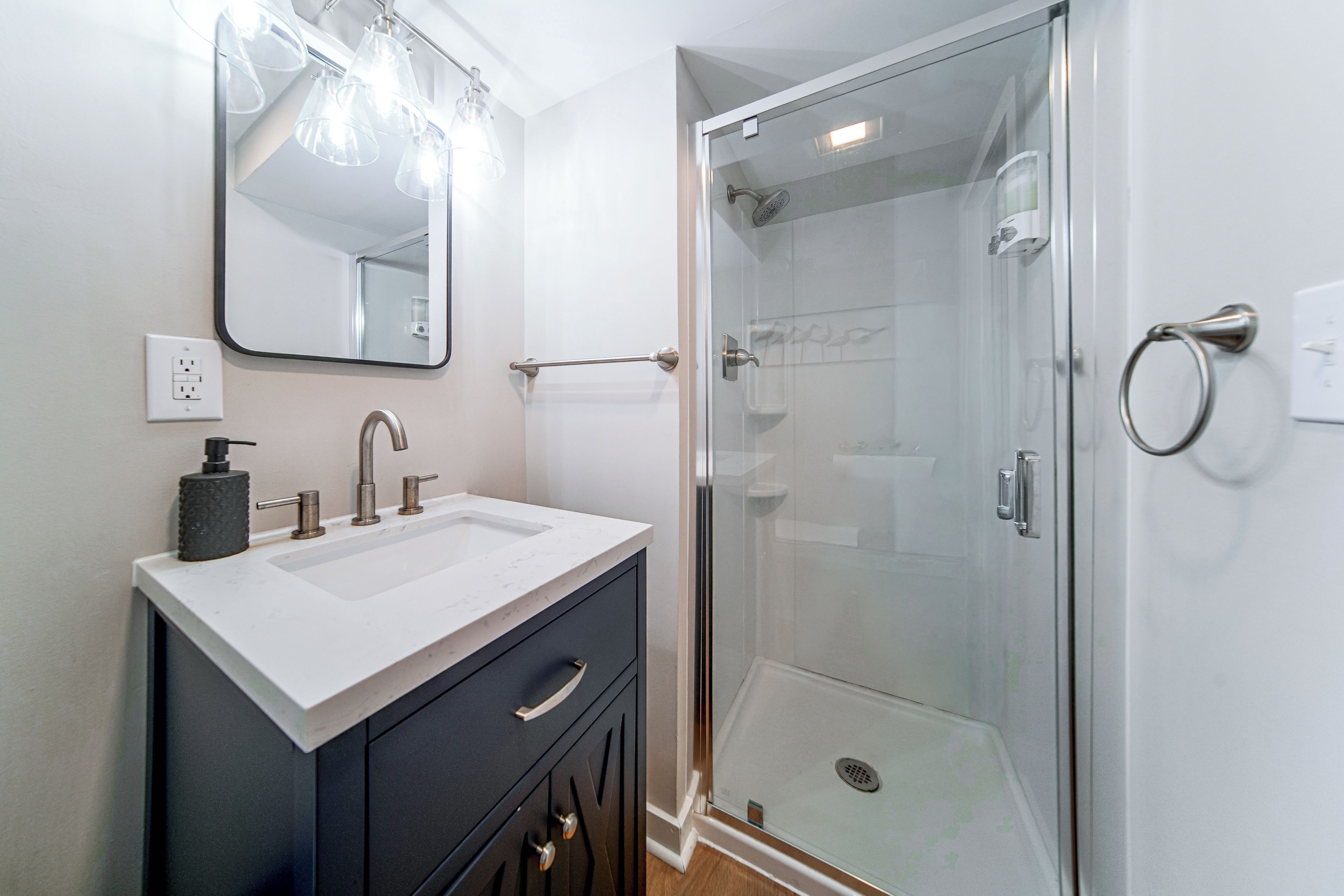 Un baño moderno con ducha envuelta en vidrio, un lavabo blanco con encimera de mármol y un espejo grande sobre el mueble.