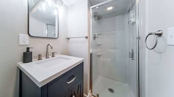 A modern bathroom with a glass-enclosed shower, a white sink with a marble countertop, and a large mirror above the vanity.