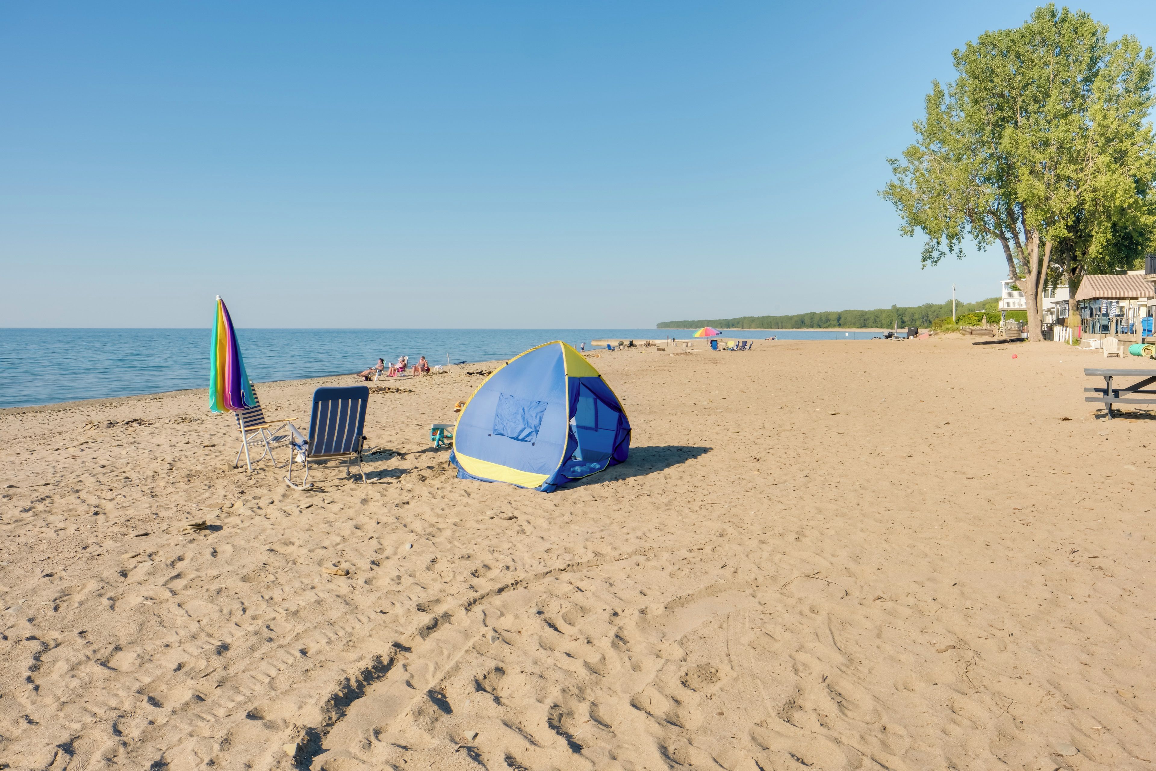 A beach with a tent, a chair, and a colorful umbrella.
