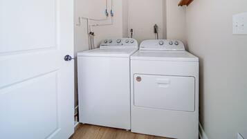 Une buanderie équipée de deux machines à laver et de deux sèche-linge Whirlpool blancs, d’un plancher en bois et d’une porte blanche.