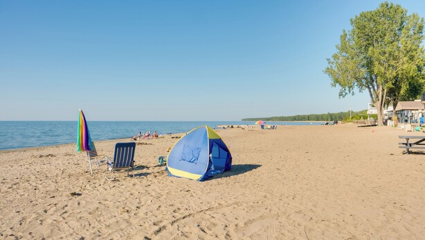 A beach with a tent, a chair, and a colorful umbrella. - 'zen Haven' Lakefront Erie Home w/ Shore Access (Erie)