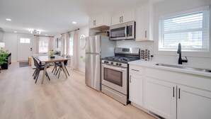 A modern kitchen with stainless steel appliances, a dining area with a wooden table and chairs, and a window with blinds. - 'zen Haven' Lakefront Erie Home w/ Shore Access (Erie)