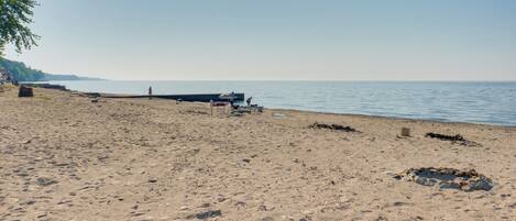 A beach with a wooden pier extending into the water, a few people, and a clear sky.