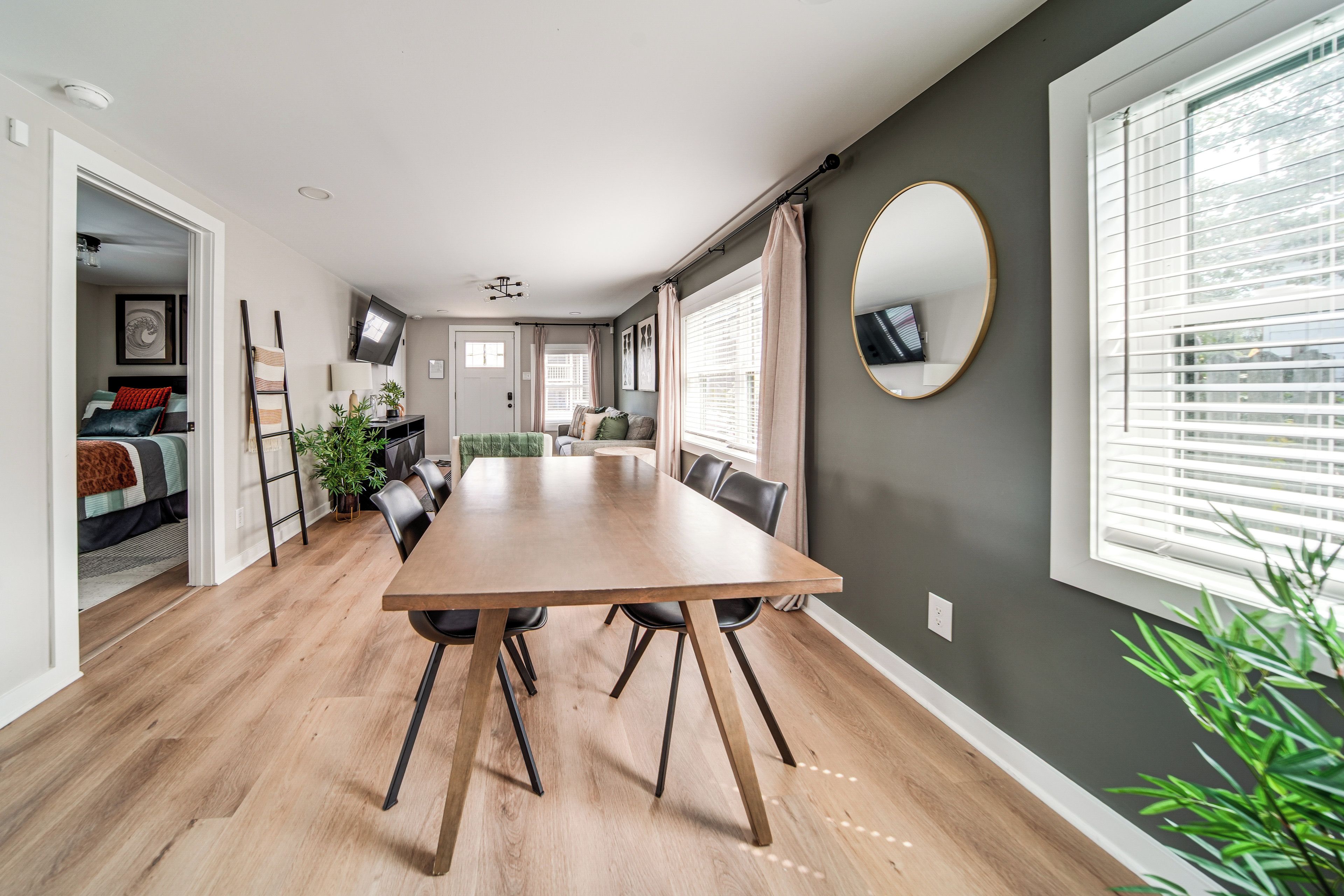 A modern living room with a wooden dining table, a sofa, and a TV mounted on the wall.