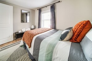 Een slaapkamer met een bed, nachtkastje, spiegel en een raam met gordijnen.