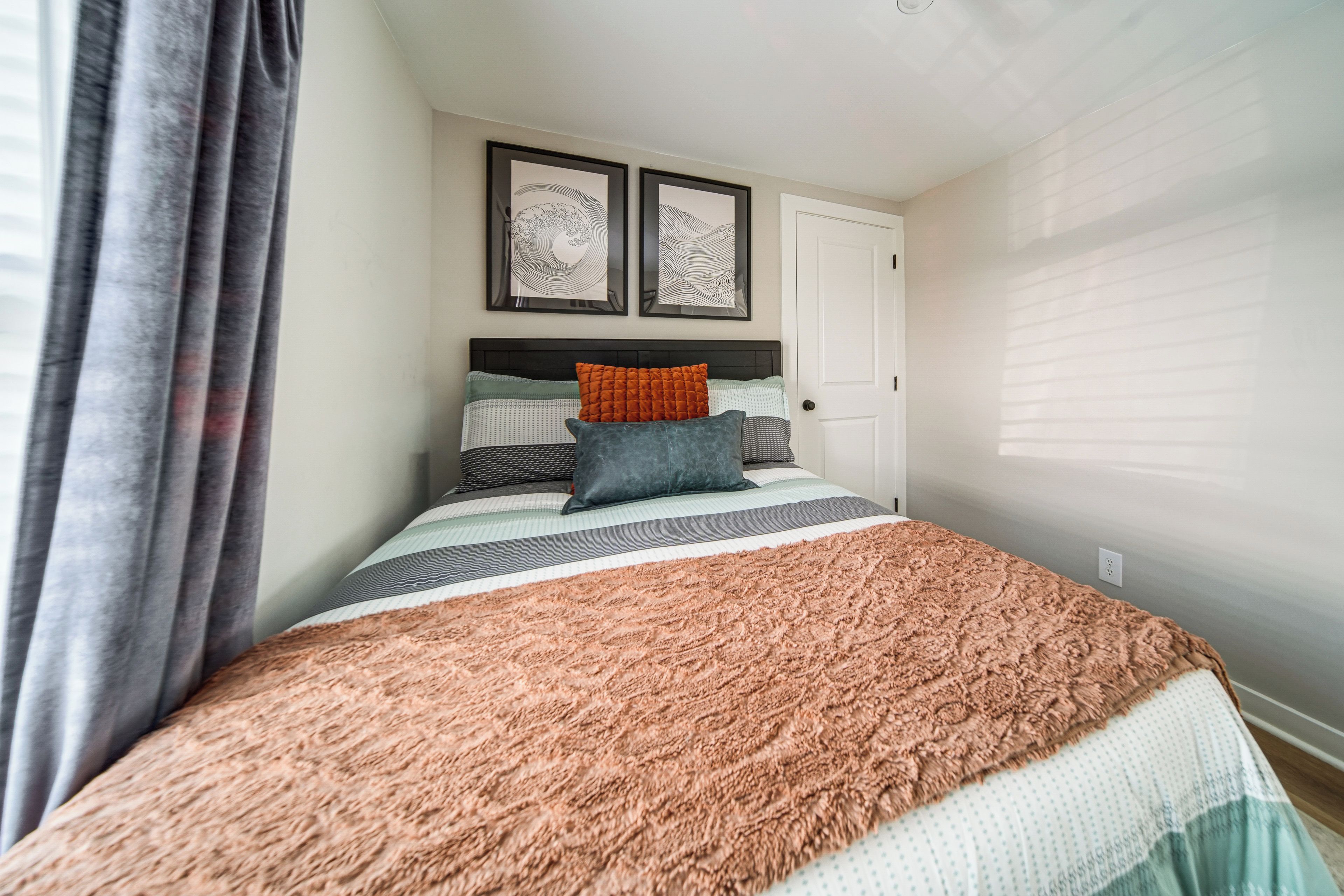 Een slaapkamer met een bed, een deur en twee kunstwerken in een lijst aan de muur.