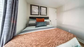 Een slaapkamer met een bed, een deur en twee kunstwerken in een lijst aan de muur.
