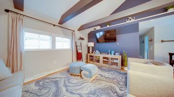 A living room with a large window, a flat-screen TV mounted on the wall, and a patterned rug.