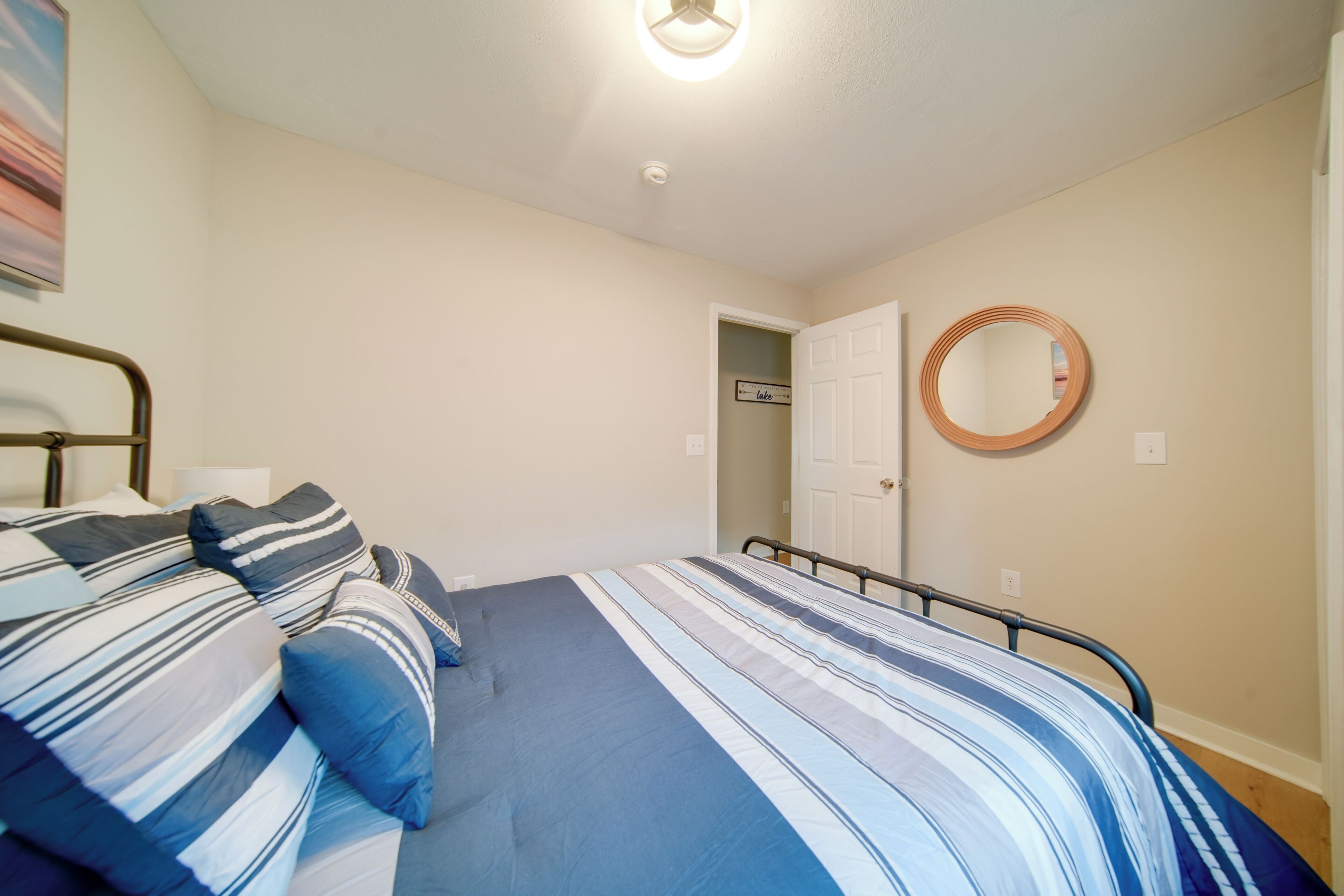 Una camera da letto con un letto, cuscini, uno specchio rotondo e una porta che dà su un'altra stanza.
