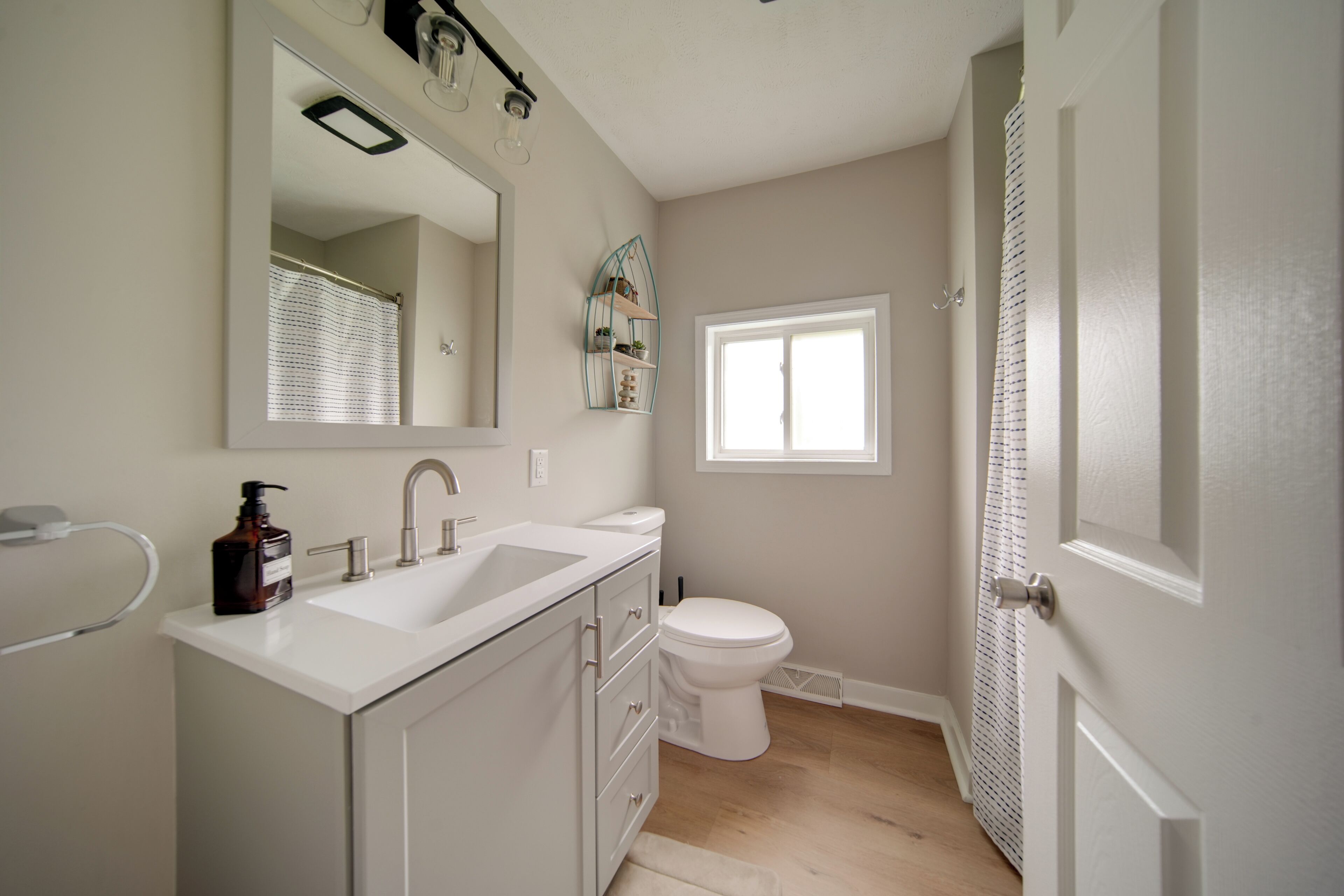 A bathroom with a white sink, a toilet, and a shower. There is a window providing natural light and a mirror above the sink.