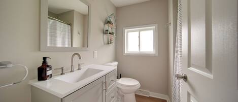 A bathroom with a white sink, a toilet, and a shower. There is a window providing natural light and a mirror above the sink.