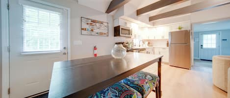Une cuisine moderne avec une table en bois foncé, un banc coloré et une grande fenêtre avec des stores.