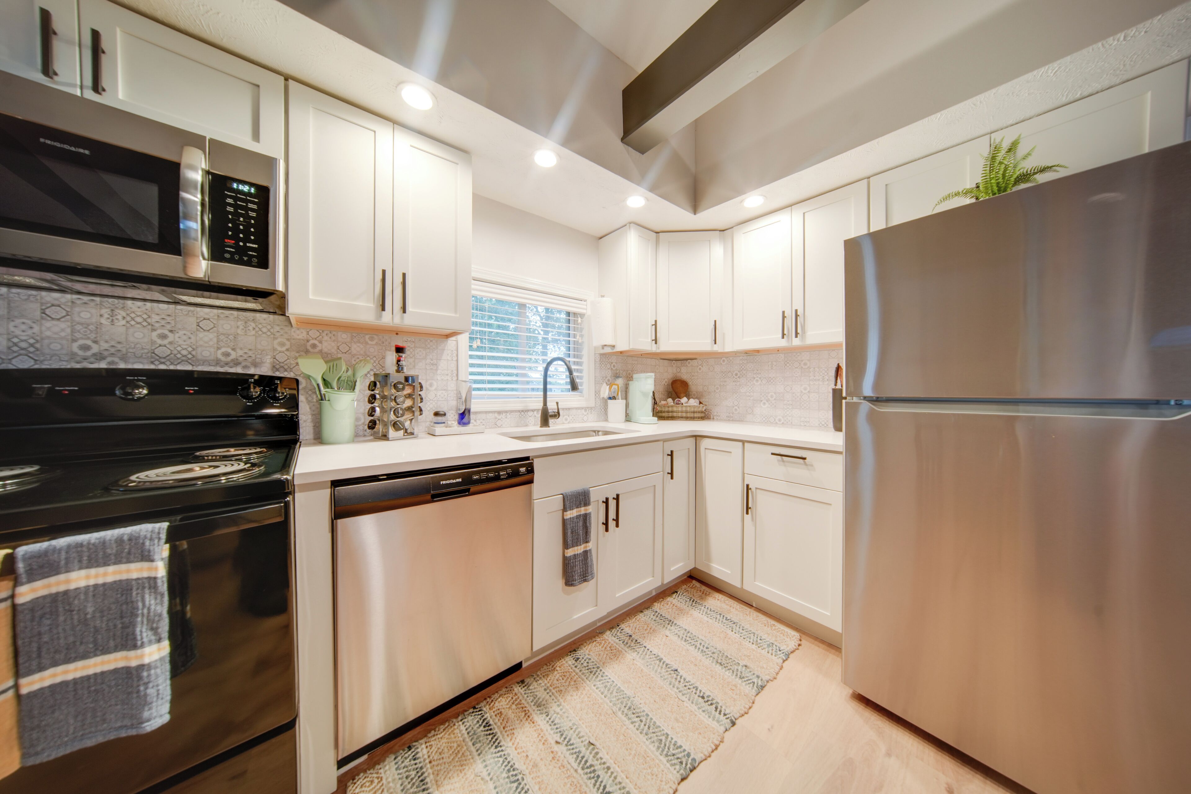 A modern kitchen with stainless steel appliances, white cabinetry, and a patterned backsplash.