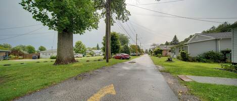 A residential street with houses on both sides, a clear road with a yellow directional arrow, and utility poles with overhead wires.