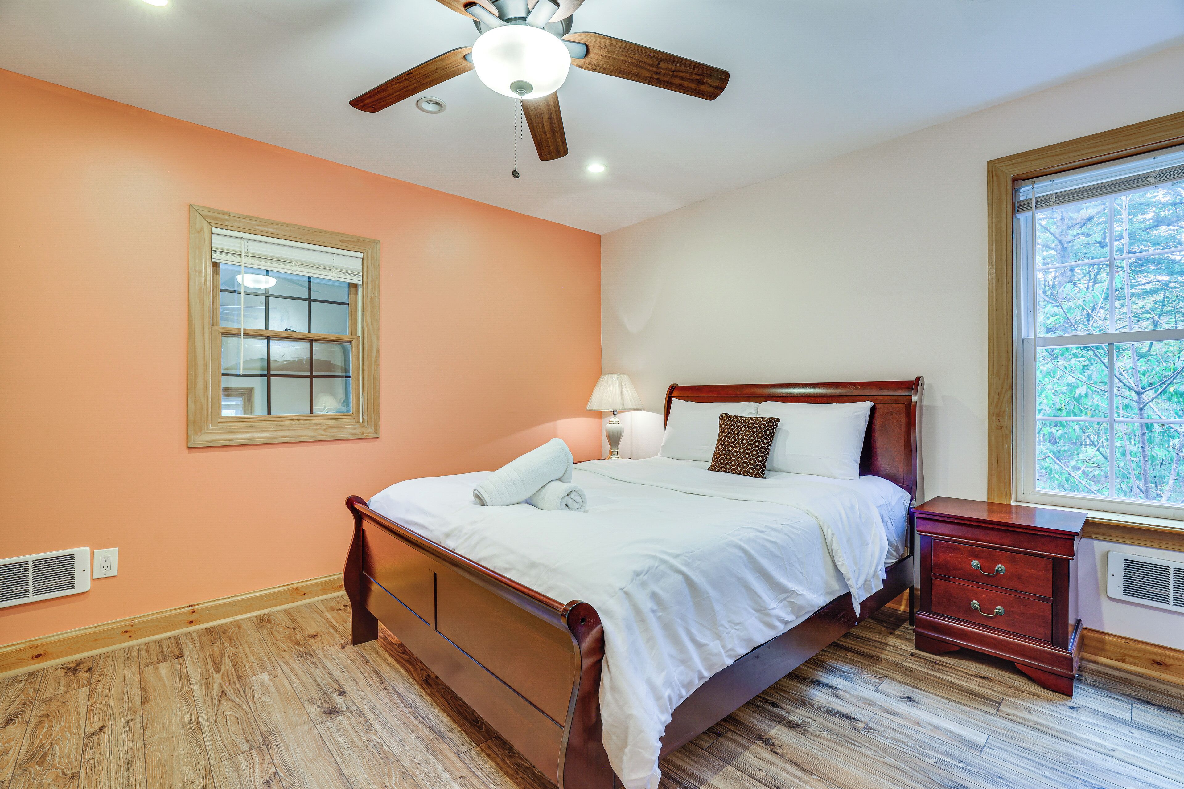 A bedroom with a wooden bed, a nightstand, a window with a view, and a ceiling fan.