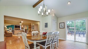 A spacious dining area with a wooden table and white chairs, a chandelier, and a view of a deck through a glass door.