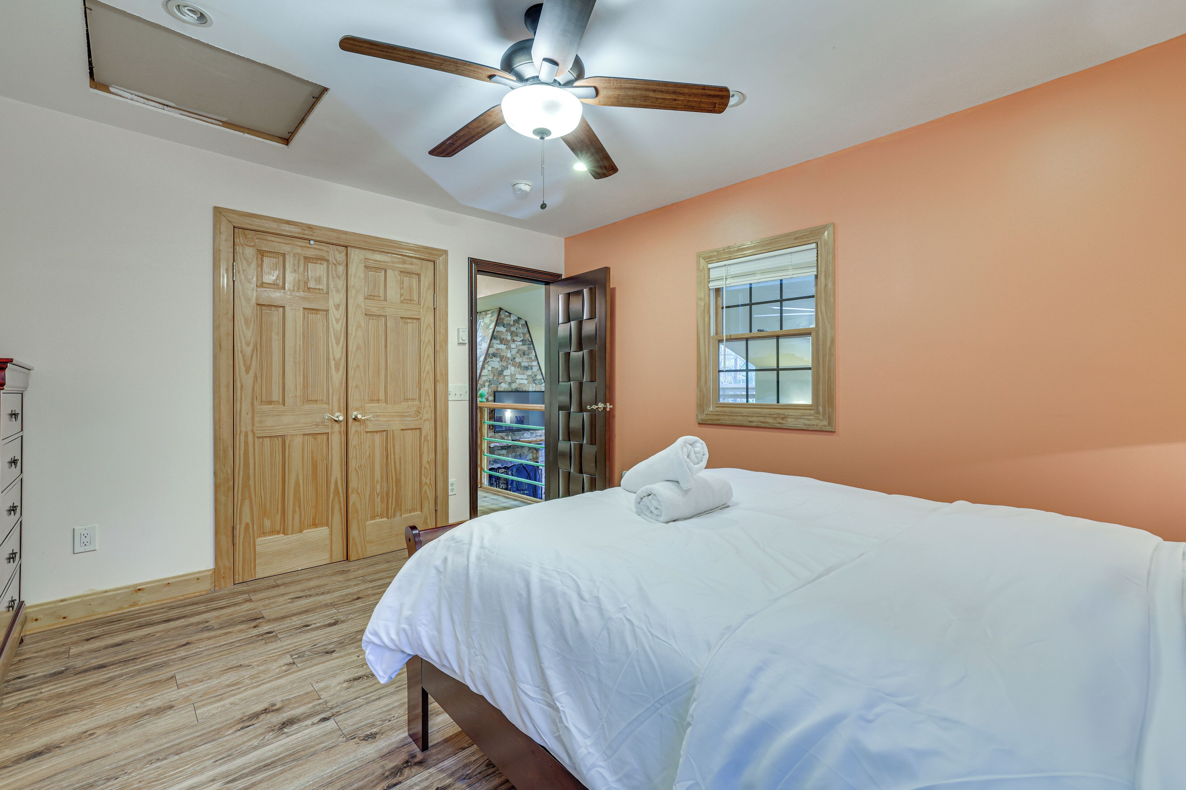 A bedroom with a bed, wooden wardrobe, ceiling fan, and a window with blinds.