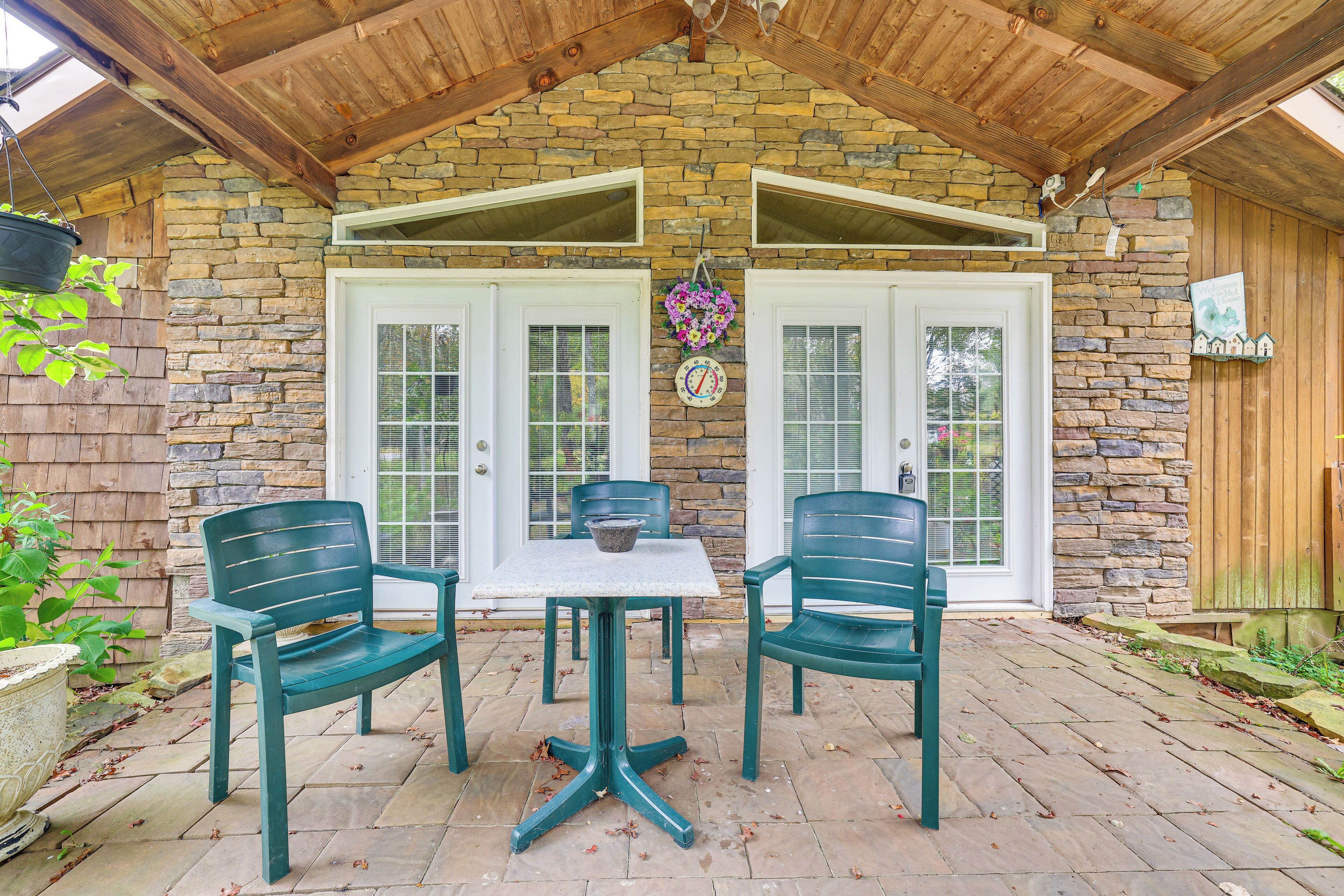 A patio with two green chairs and a table, a stone wall, and a wooden ceiling.