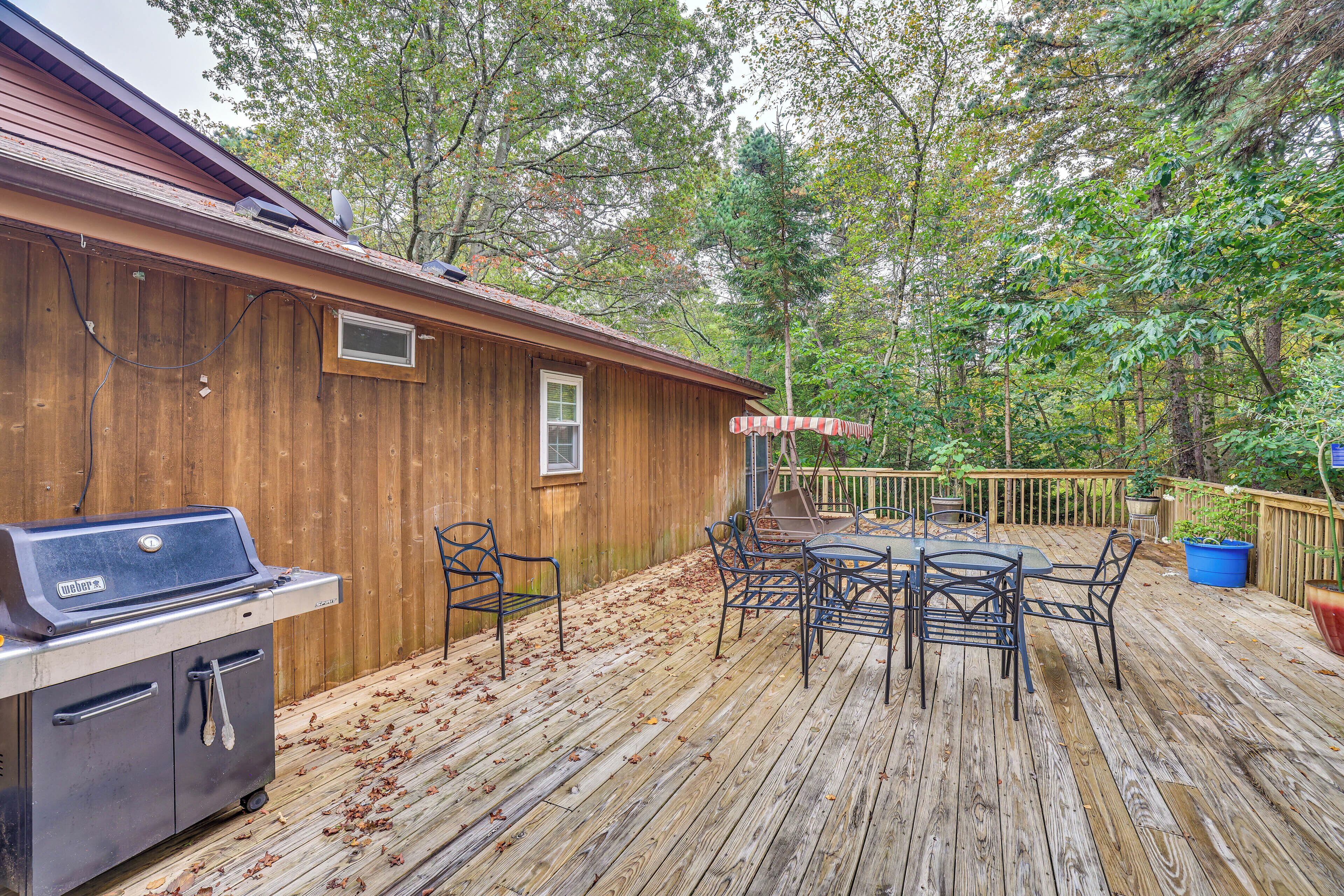 A wooden deck with a barbecue grill, outdoor furniture, and a wooden building in a wooded area.