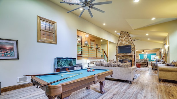 A spacious living room with a pool table, comfortable seating, and a stone fireplace.