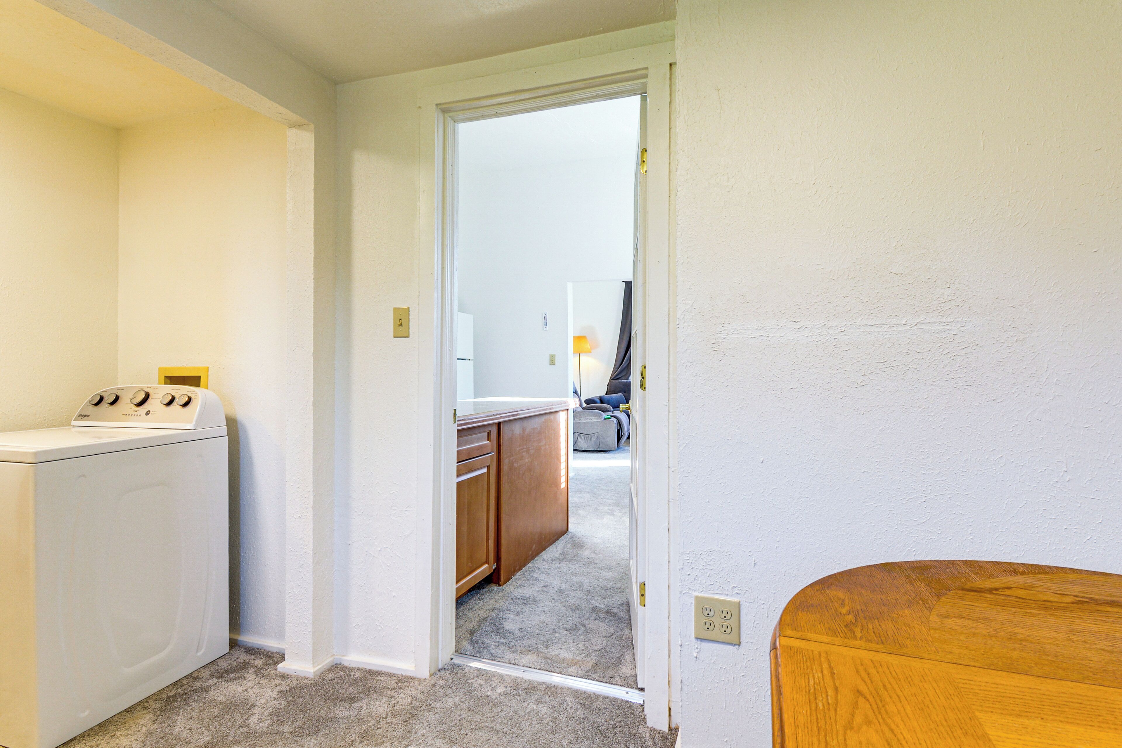 A laundry area with a washing machine, a wooden cabinet, and a doorway leading to a kitchen area.