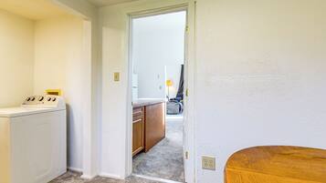 A laundry area with a washing machine, a wooden cabinet, and a doorway leading to a kitchen area.