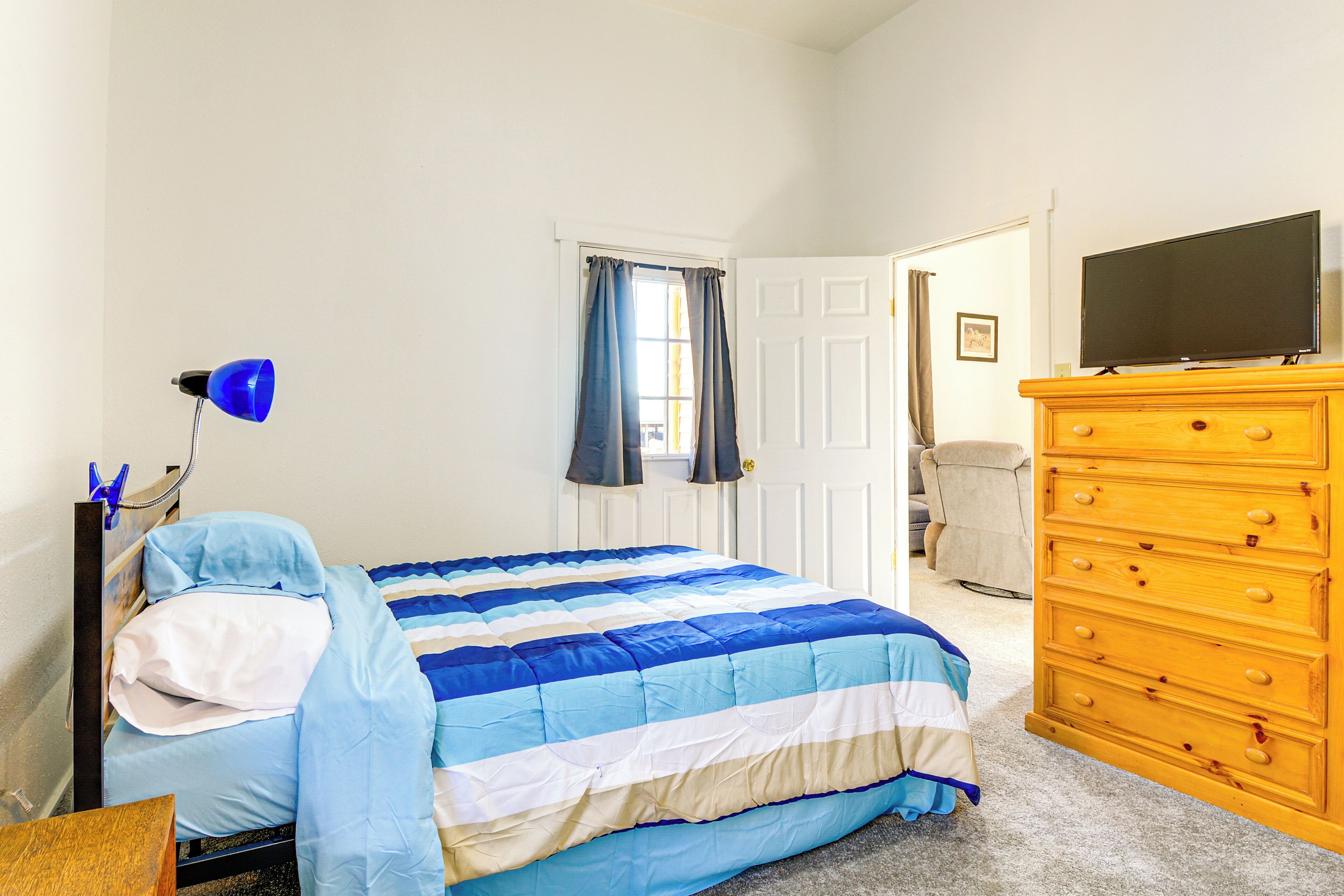A bedroom with a bed, a dresser, a television, and a window with curtains.