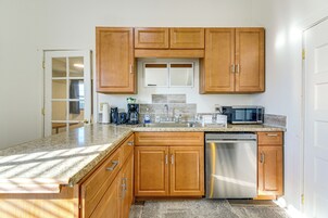 Una cocina con gabinetes de madera, lavavajillas de acero inoxidable, microondas y encimera de granito.