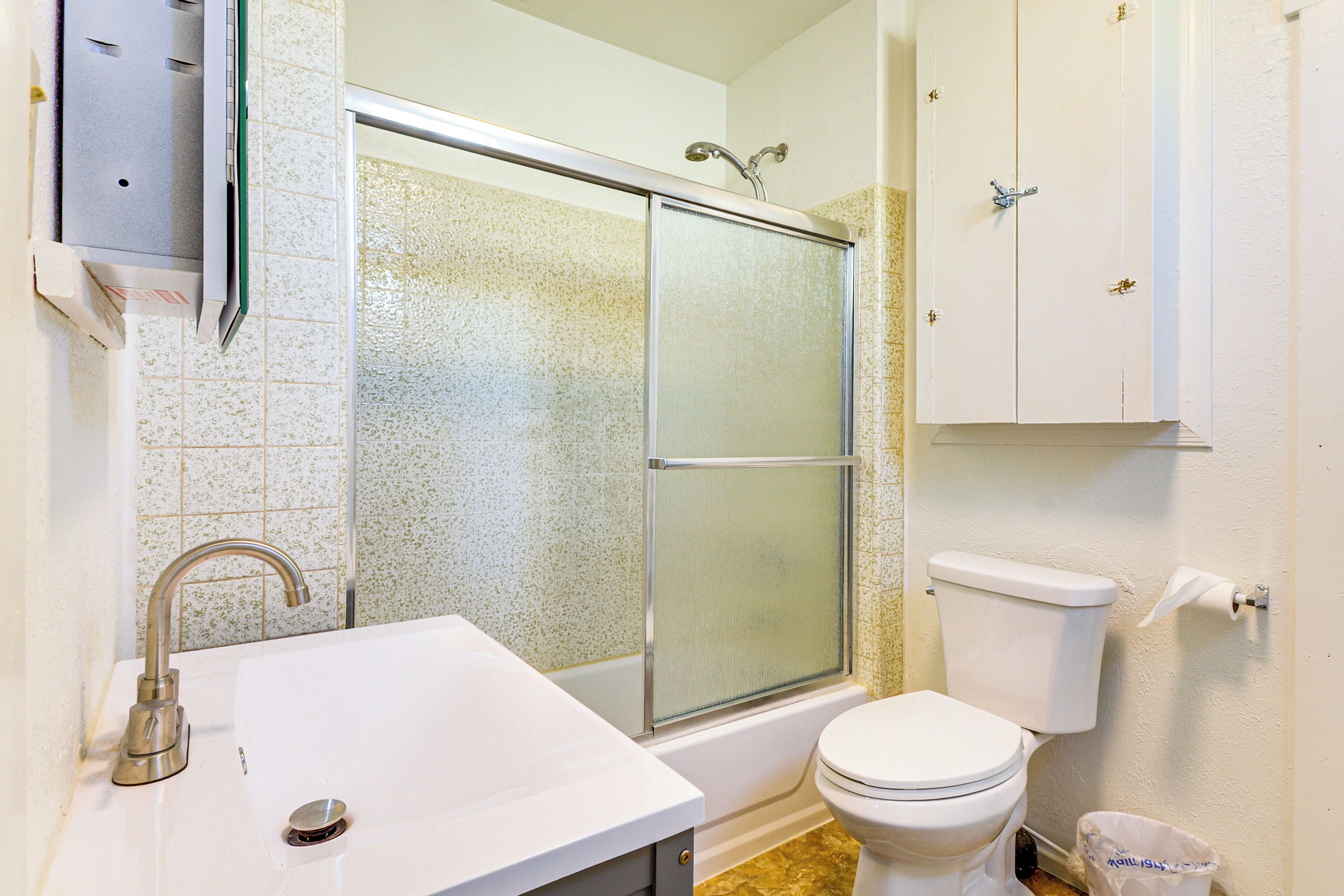 A bathroom with a shower, toilet, sink, and cabinets.