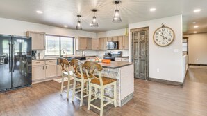 A modern kitchen with wooden cabinets, a built-in island with chairs, a refrigerator, and a wall clock. - Deck & Hot Tub: Group Golf Retreat in Sturgis (Sturgis)