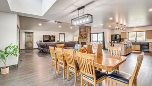 A spacious kitchen with wooden cabinets, a dining area with a large wooden table and chairs, and a cozy living area with a sofa and fireplace. - Deck & Hot Tub: Group Golf Retreat in Sturgis (Sturgis)